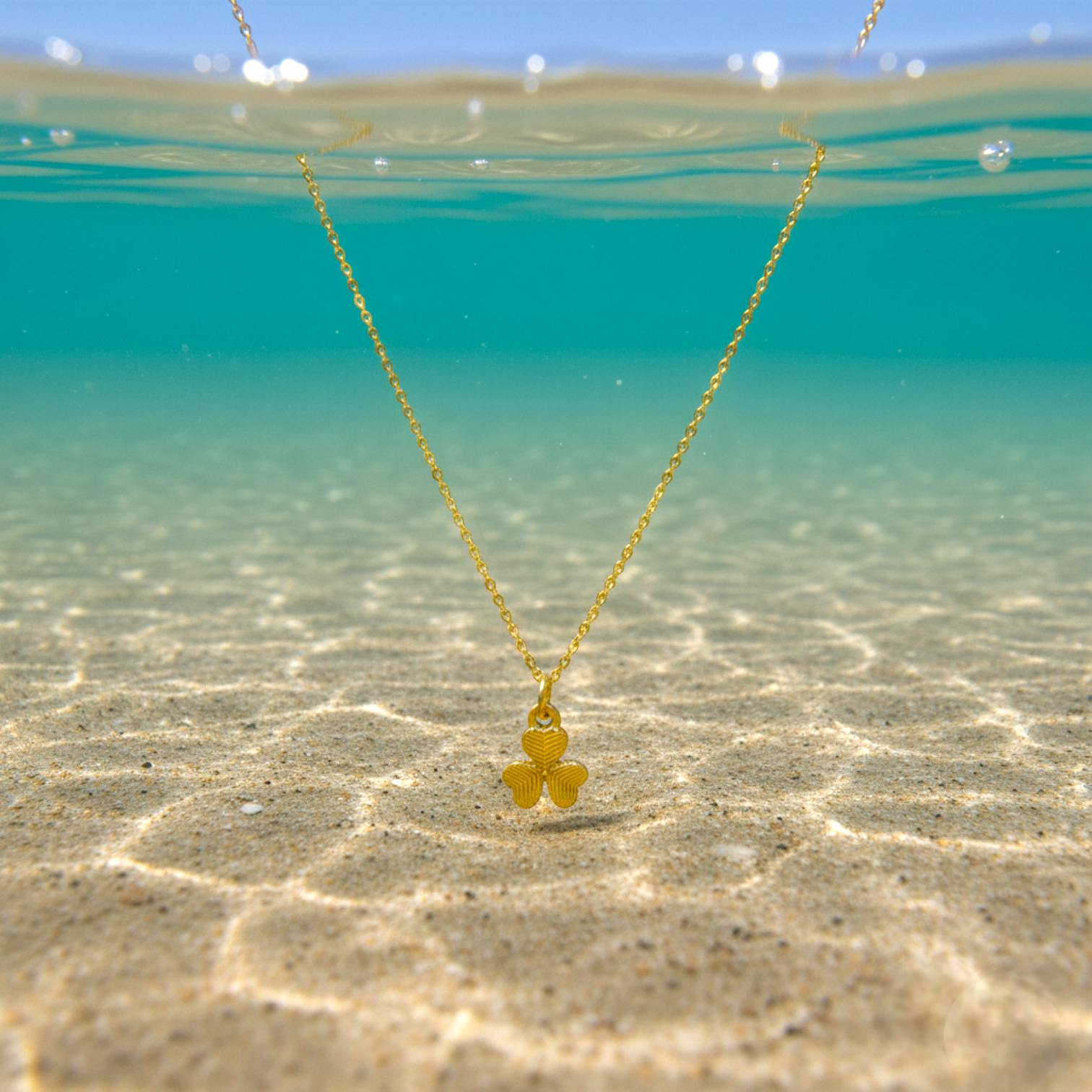 Gold necklace with a clover pendant floating in clear water.