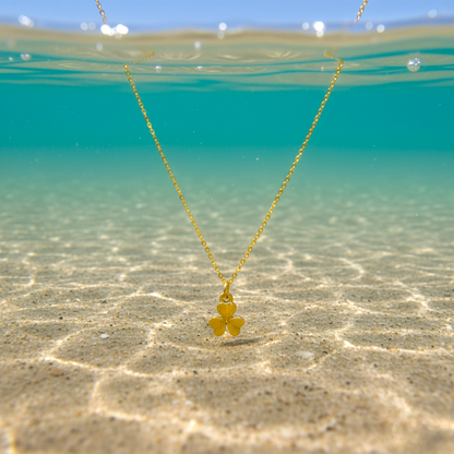 Gold necklace with a clover pendant floating in clear water.